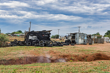 Fototapeta premium informal settlement, or shanty town, built with corrugated iron sheets and discarded tires, makeshift housing and smoking ditch