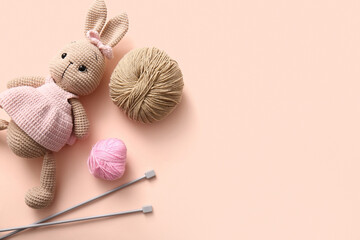 Knitted bunny toy with yarn and knitting needles on beige background