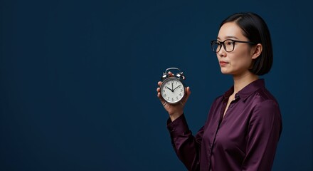 Professional asian woman holding a classic alarm clock. Business concept of time management and deadlines. Studio shot with copy space