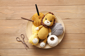 Knitted lion toy with yarn, scissors and crochet hooks on wooden background