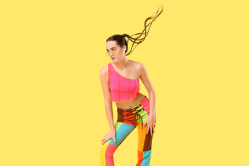 Pretty young woman with braids in earphones dancing on yellow background