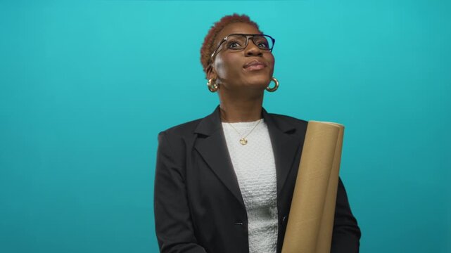 African american architect holds rolled blueprint and looks aside in a bright turquoise studio; ambition.