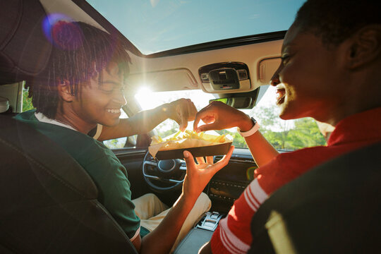 Happy friends sharing french fries during road trip in car