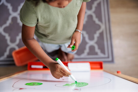 Child drawing with green marker on whiteboard.