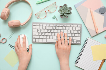Female hands with computer keyboard, mouse and office stationery on turquoise background