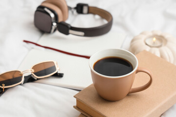 Cup of coffee with books and sunglasses on bed, closeup