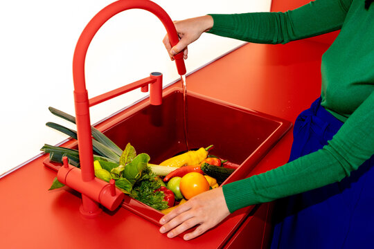 Person washing fresh vegetables in modern red sink