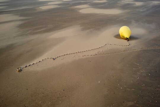 Bright Yellow Buoy on Sandy Beach With Traces in the Sand