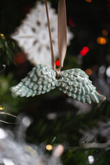 Ceramic toy in the form of a snowflake hanging on a Christmas tree with lights from a garland in the background.