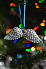 Ceramic toy in the form of a snowflake hanging on a Christmas tree with lights from a garland in the background.
