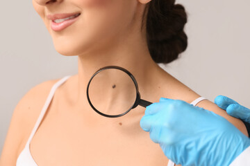 Dermatologist with magnifying glass examining moles of young woman on white background, closeup