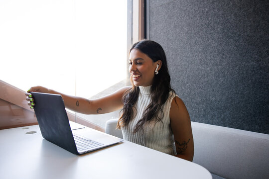 Smiling woman using laptop in modern workspace for video conference