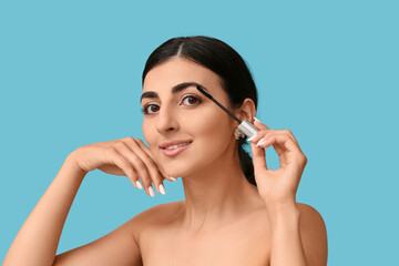 Fototapeta premium Pretty young woman with mascara brush on blue background