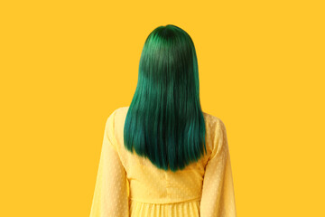 Young woman with green hair on yellow background, back view