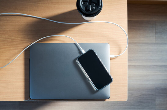 Top view of charging phone on laptop with coffee on desk