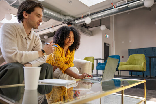 Two coworkers collaborate on a laptop in a modern office lounge