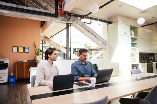 Two professionals collaborating on laptops in a stylish modern office