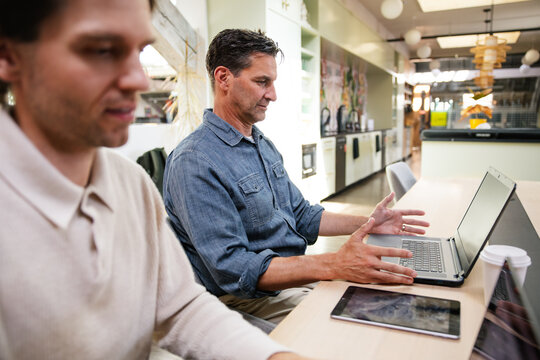 Two men collaborating in a modern office setting with laptops 