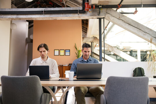 Two coworkers working on laptops in a modern industrial-style office