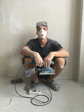 Man in respirator squatting with electric sander during renovation
