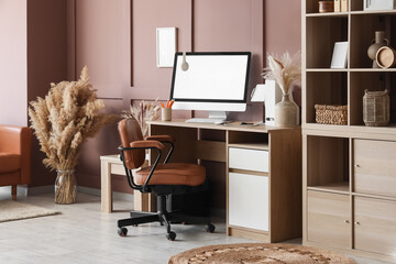 Interior of modern office with workplace, shelving unit and pampas grass near brown wall