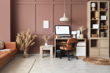 Interior of modern office with workplace, shelving unit and sofa near brown wall