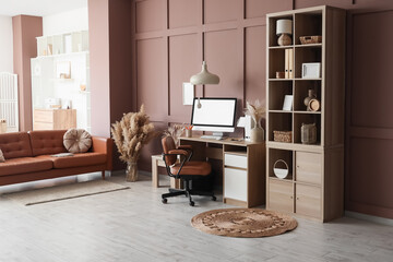 Interior of modern office with workplace, shelving unit and sofa near brown wall