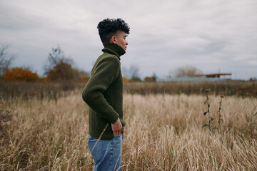 Side profile of a young man standing in tall autumn grass, candid pose and natural expression...