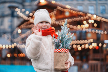 Child holding small Christmas tree at festive market during winter season