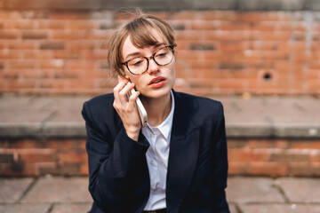 Young woman in formal attire speaks on the phone while sitting on outdoor steps during daytime