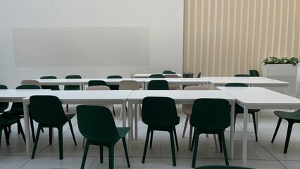  Modern empty classroom or meeting room with white tables and green chairs, blurred abstract background for educational and business concepts