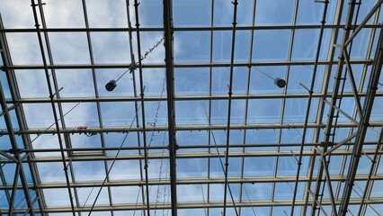 Modern glass and steel roof structure with a clear blue sky and clouds, architectural background for construction, engineering, and design concepts