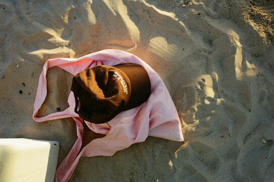 Brown hat resting on a pink bag on sandy beach