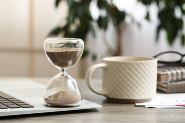 Fototapeta premium Hourglass with laptop and cup of coffee on table in office
