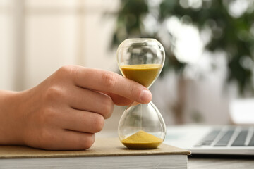 Businesswoman with hourglass, book and laptop at table in office, closeup
