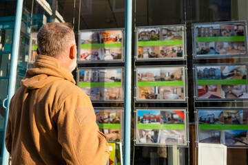 Man browsing property listings in a real estate window display in the city during the afternoon