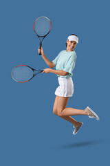 Happy young female tennis player with rackets jumping on blue background