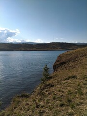 Fototapeta premium A sunny slope over calm water and distant hills. Clear sky, natural scenery, summer atmosphere and tranquility.