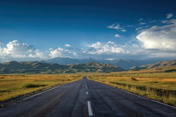 Naklejka premium Scenic Country Road Leading to Distant Mountains under Blue Sky with Puffy Clouds on Sunny Day at Dusk Perspective View