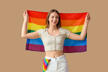 Happy young woman with LGBT flag on beige background