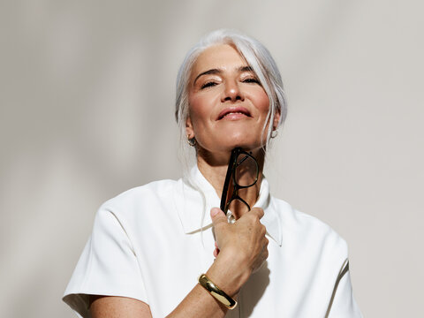 Confident Woman With Gray Hair Holding Glasses and Smiling