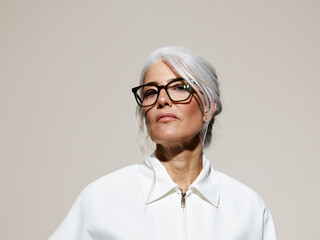 Woman With Long Silver Hair and Glasses Poses in a Sleek White Outfit