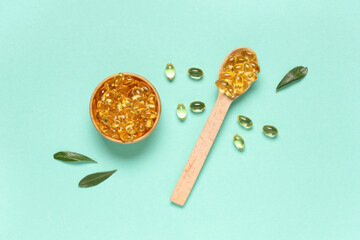 Wooden bowl and spoon with vitamin E capsules on turquoise background