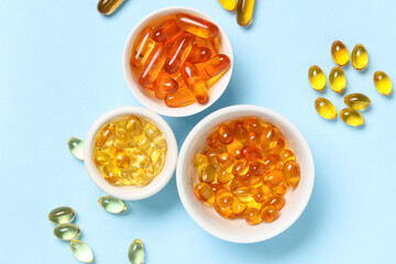 Bowls with vitamin E capsules on blue background
