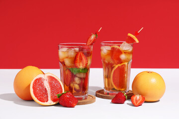 Fototapeta premium Glasses of tasty cold ice tea with strawberry and grapefruit on white table near red wall