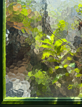 Sunlight Filtering Through Textured Glass With Green Leaves Outside