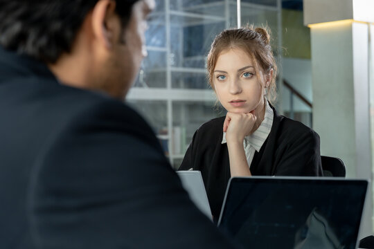 young asian male professional speaking during business meeting in office with caucasian woman and male coworkers using laptops for project communication and teamwork in multiracial collaboration