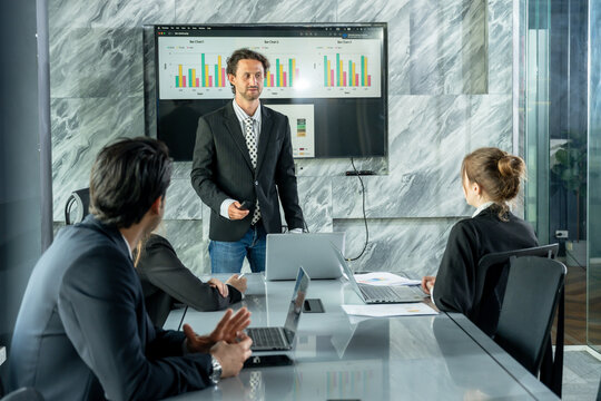 Office business presentation with caucasian man presenting financial charts to multiracial team in meeting room during corporate discussion showing teamwork and business collaboration