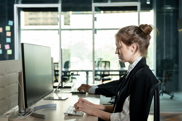 Young caucasian female employee typing on keyboard while working in office using desktop computer in professional workspace representing business task execution and office work productivity