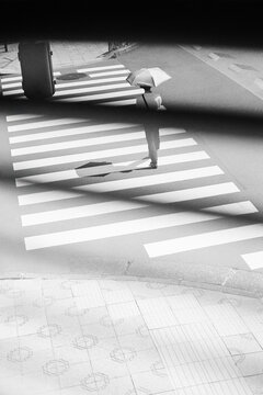 Person crossing street with umbrella seen through window blinds
